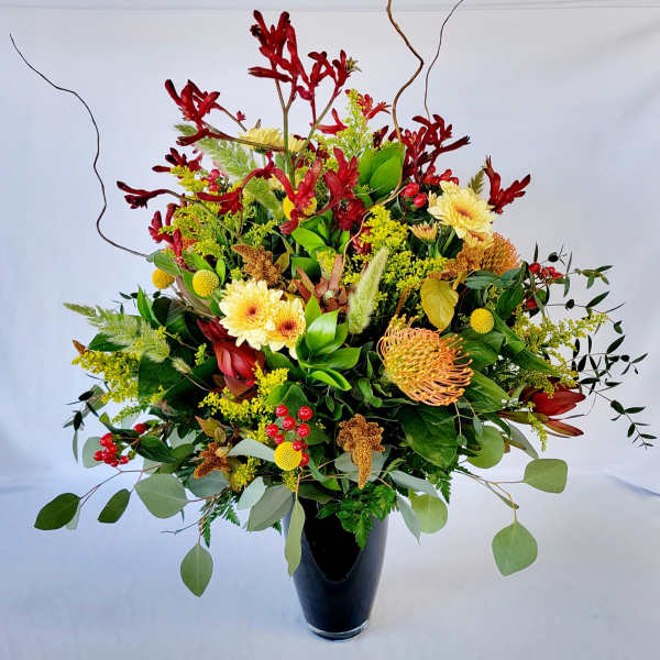 Large mixed floral arrangement in a black vase with red, yellow, and green blooms