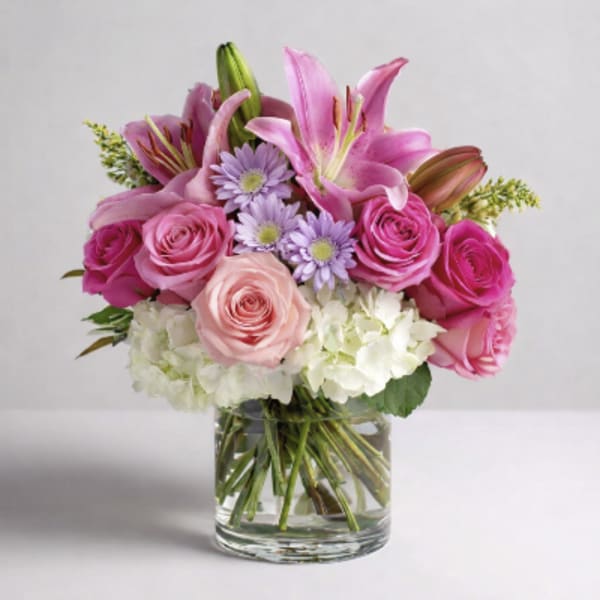 Pink lilies, roses, and lavender daisies in a clear glass vase