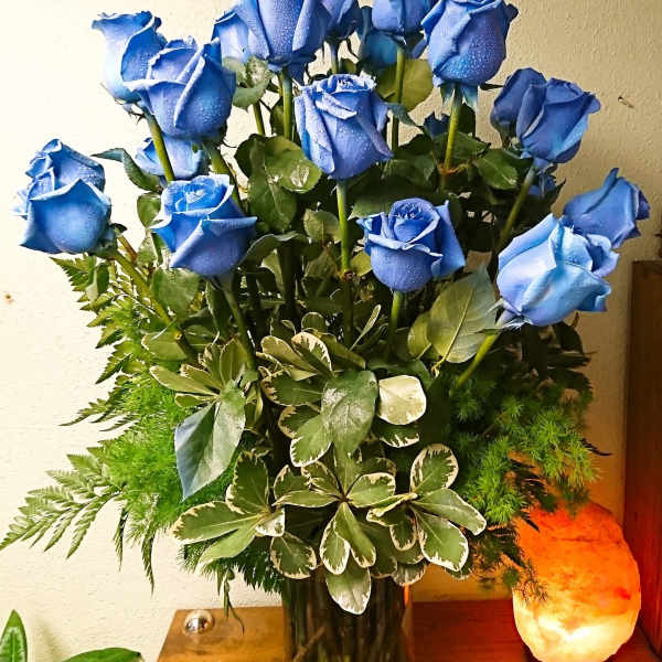 Blue roses arranged in a glass vase with mixed greenery