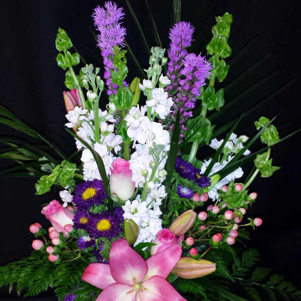 Pink lilies and purple flowers in a glass vase with a purple ribbon