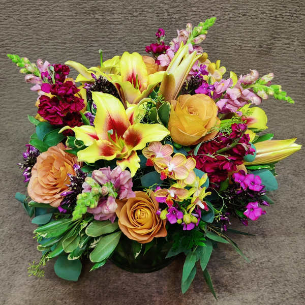Mixed bouquet with yellow lilies, peach roses, and pink flowers in a low vase