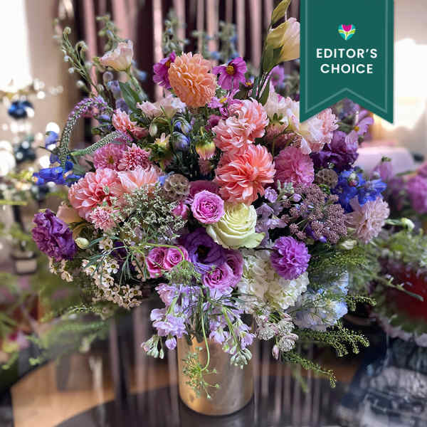 Mixed pink, purple, and peach flowers in a gold vase