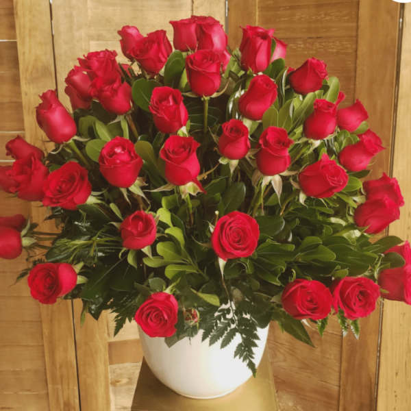 Large arrangement of red roses in a white ceramic pot against a wood background