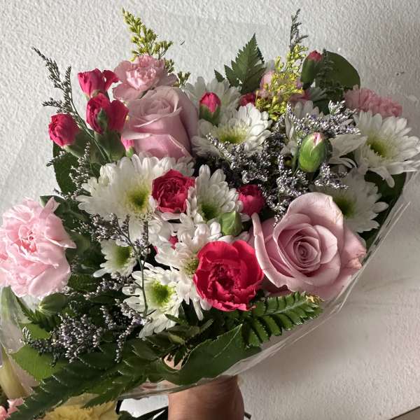 Bouquet of pink roses, carnations, and white daisies wrapped in clear plastic