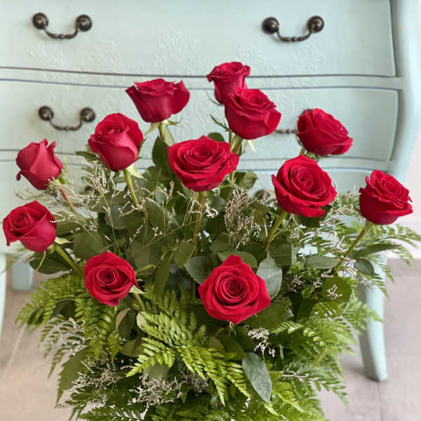 Red roses arranged in a clear glass vase with fern foliage
