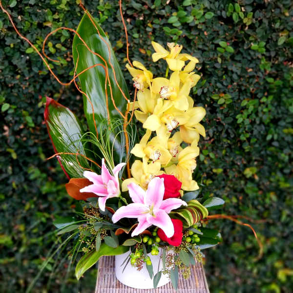 Tropical flower arrangement with yellow orchids and pink lilies in a white container