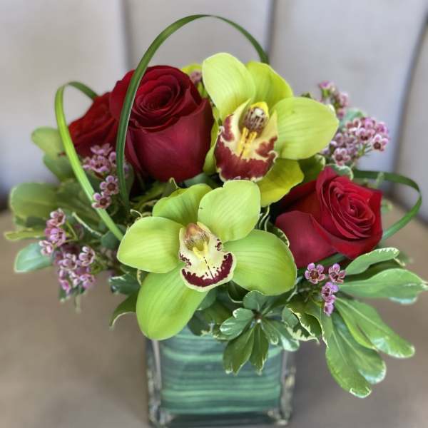 Red roses and green orchids arranged in a square glass vase