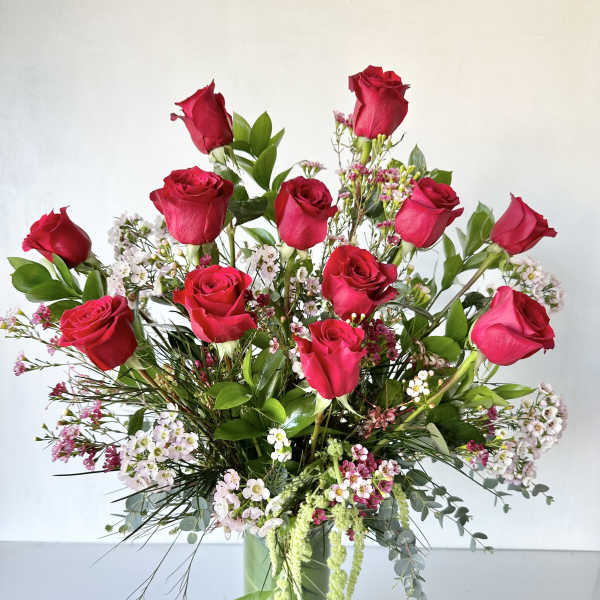 Tall bouquet of red roses and small pink-white filler flowers in a glass vase