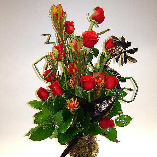 Tall bouquet of red roses and tropical flowers in a glass vase