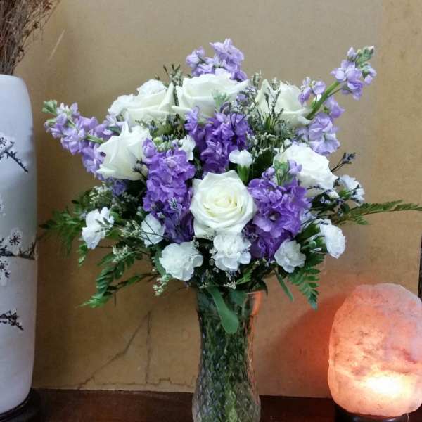 White roses and purple flowers arranged in a glass vase
