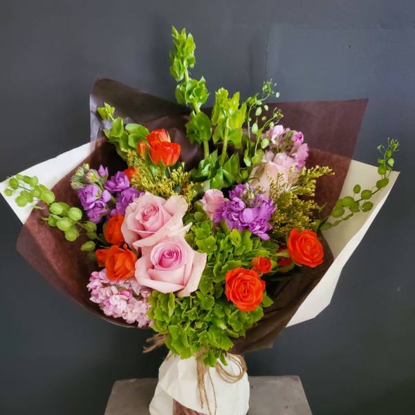 Bouquet of pink and orange roses with purple blooms and green filler