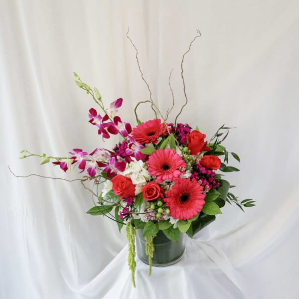 Bouquet of pink gerbera daisies, red roses, and purple orchids in a glass vase