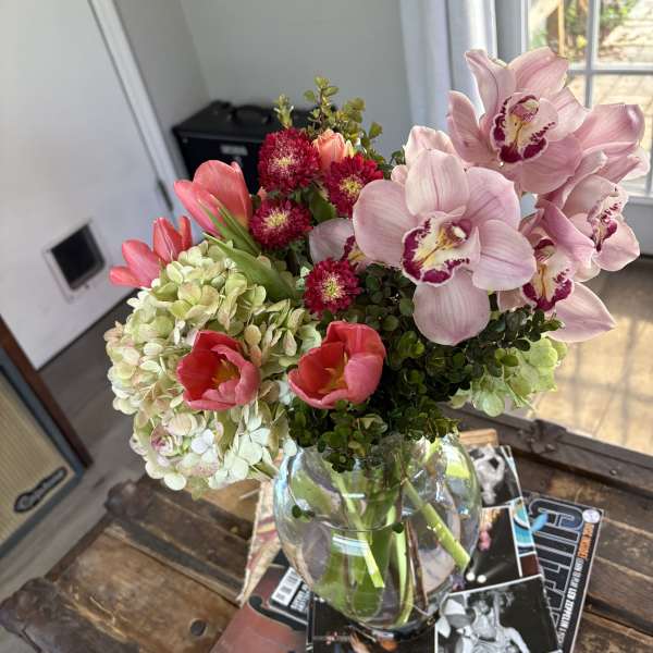 Bouquet of pink orchids, tulips, hydrangeas, and red blooms in a glass vase