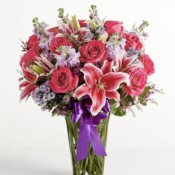 Pink roses and lilies in a clear glass vase with a purple ribbon