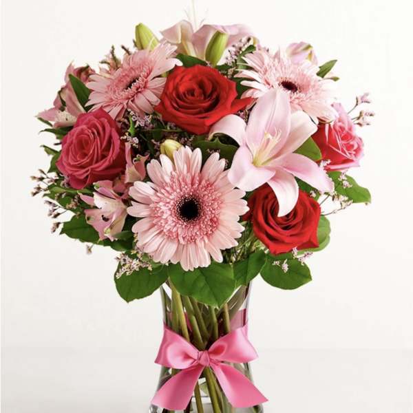 Pink and red flower bouquet in a glass vase with a pink ribbon