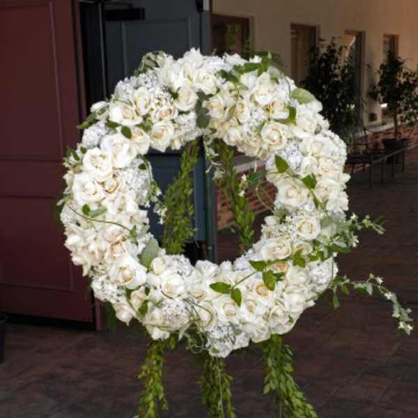 Large white floral wreath on an easel with trailing greenery