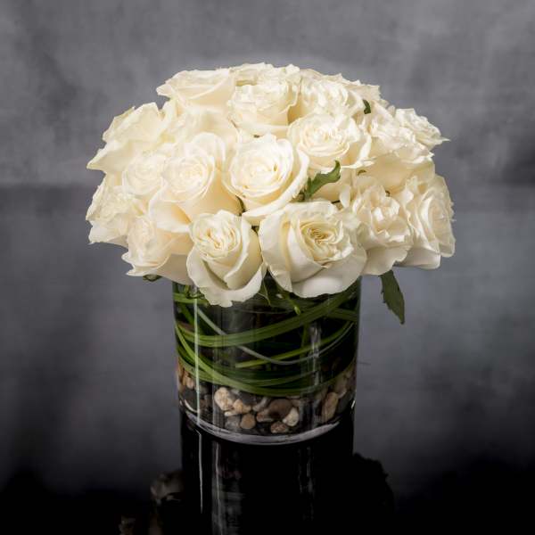 Compact arrangement of white roses in a clear glass cylinder vase with stones at the base