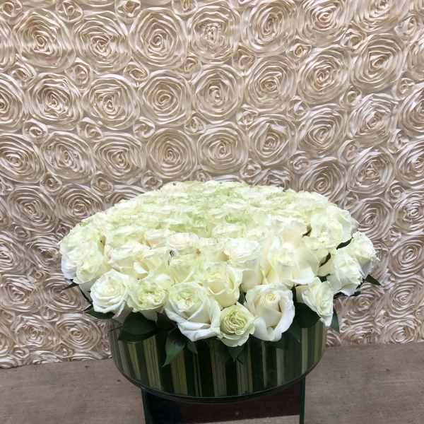 Large white rose arrangement in a glass vase on a mirrored stand