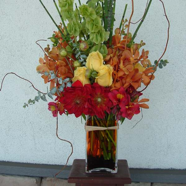 Tall mixed bouquet in a glass vase with red, yellow, orange, and green flowers