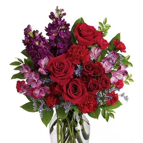 Red roses and purple flowers arranged in a clear glass vase