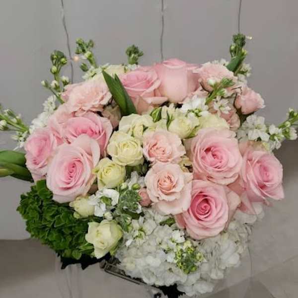 Round arrangement of pink and cream roses with white hydrangeas on a clear stand