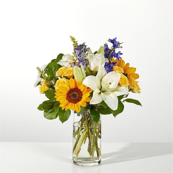 Bouquet of sunflowers, white lilies, and blue flowers in a glass vase