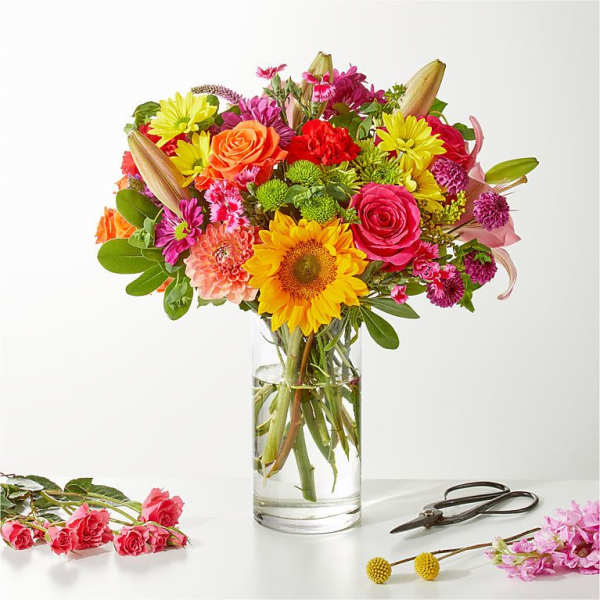 Colorful mixed bouquet in a clear glass vase with scissors and loose flowers nearby