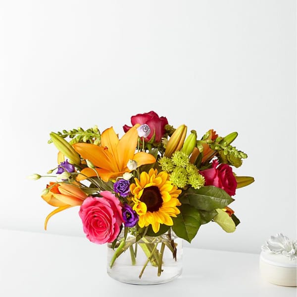 Mixed bouquet of roses, lilies, and a sunflower in a glass vase