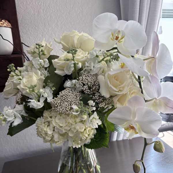 White roses, hydrangeas, and orchids arranged in a glass vase