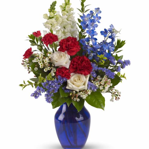 Mixed bouquet of red carnations, white roses, and blue flowers in a cobalt vase