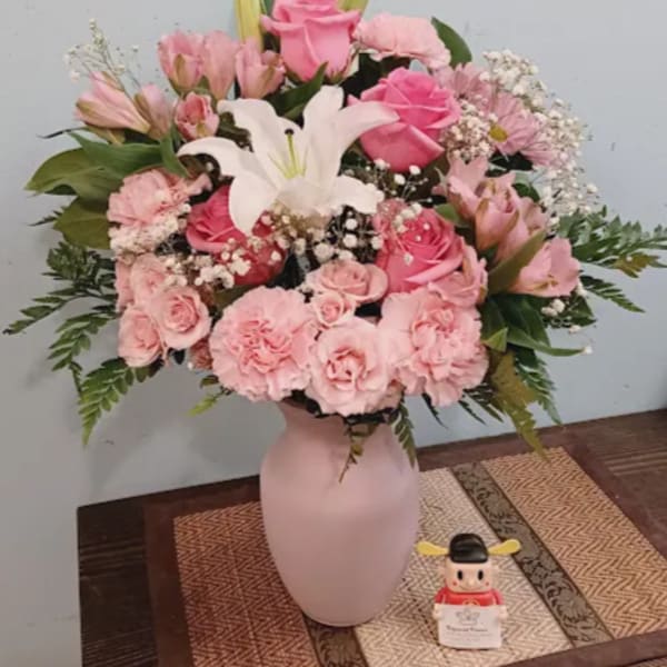 Pink and white floral arrangement in a pale vase with a small figurine beside it
