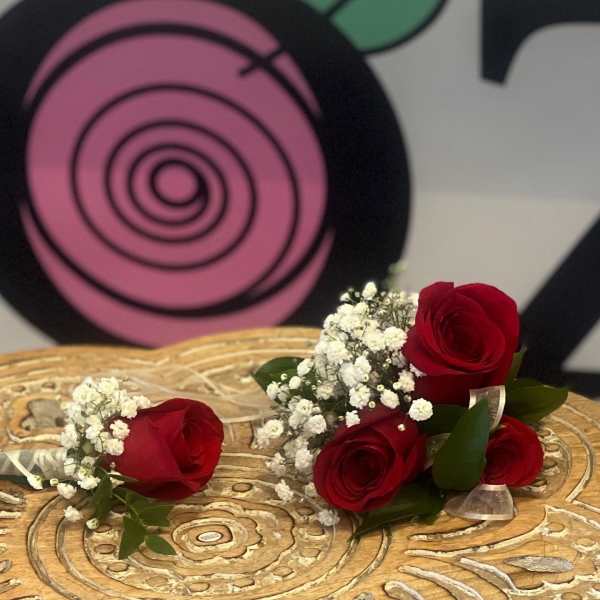 Two red rose boutonnieres with white filler flowers resting on a carved wooden surface