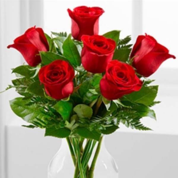 Medium bouquet of red roses arranged with foliage in a clear glass vase