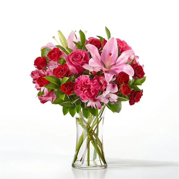 Pink lilies and red roses arranged in a clear glass vase