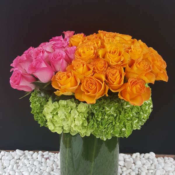 Pink and orange roses arranged in a tall glass vase