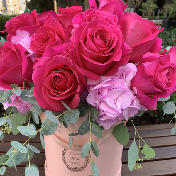 Hot pink roses and pale pink hydrangea in a blush hatbox with trailing eucalyptus.