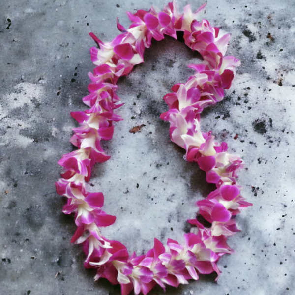 Purple and white orchid flower lei arranged in an oval on a gray stone surface
