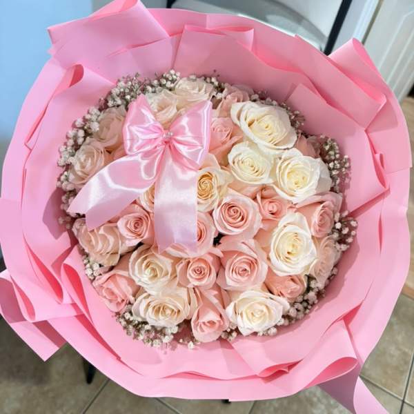 Pink-wrapped bouquet of pale pink and white roses with a satin bow