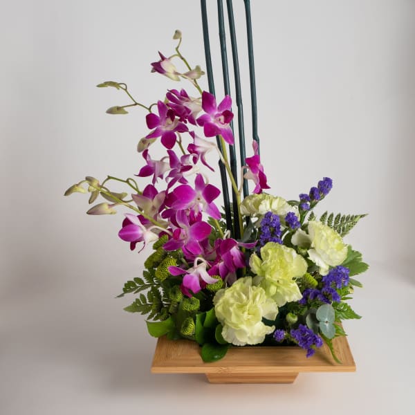 Purple orchids and pale carnations in a wooden container