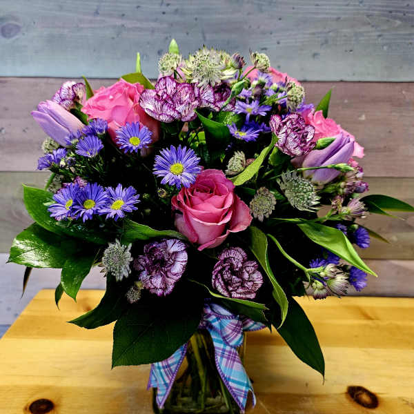 Bouquet of pink roses, purple daisies, and carnations in a glass vase