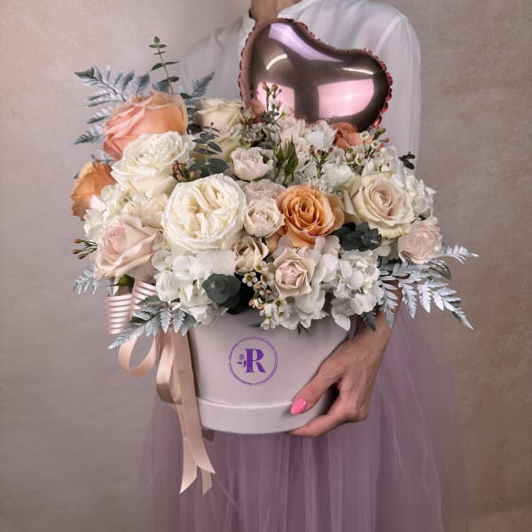 Round hatbox arrangement of cream and peach roses with white hydrangeas and a pink heart balloon
