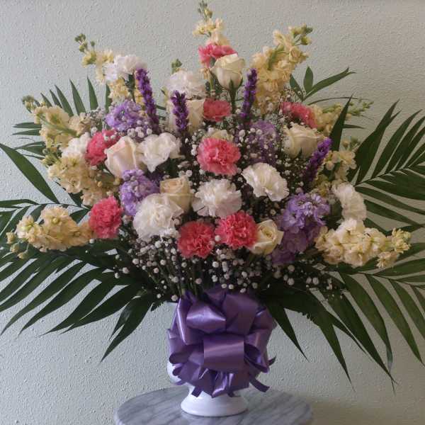Mixed bouquet of carnations and roses in a white vase with a purple ribbon