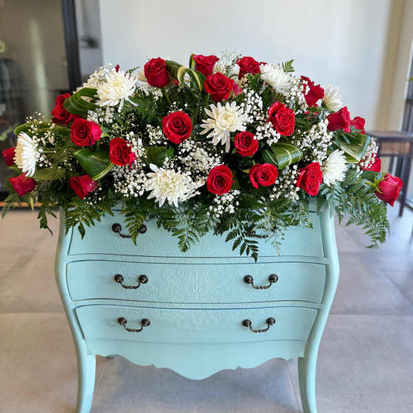 Red roses and white daisies arranged on a light blue dresser