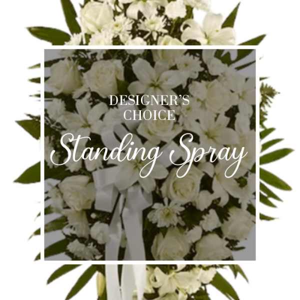 White standing spray of roses, lilies, and other flowers with a white ribbon bow