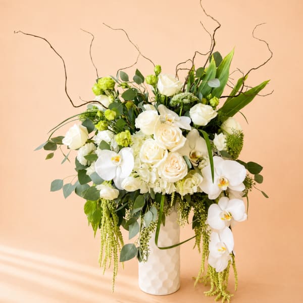 White roses and orchids in a tall white vase with greenery