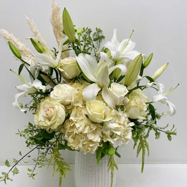 White lilies and roses arranged in a tall white vase