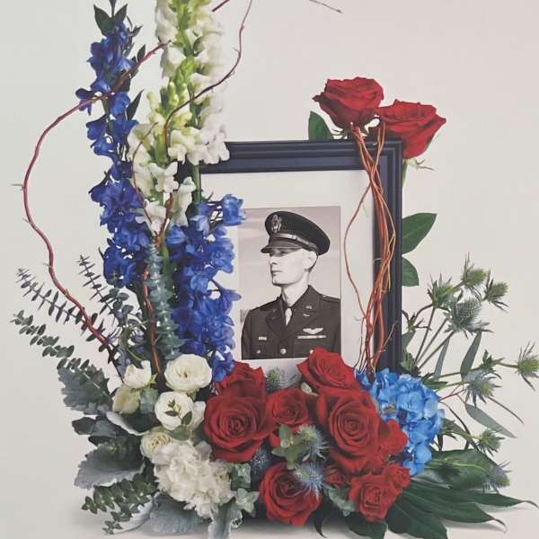 Floral tribute around a framed black-and-white portrait with red roses and blue-white flowers