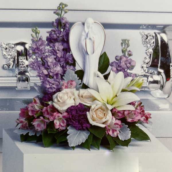 Purple and pink floral arrangement with white lilies and roses in a silver casket