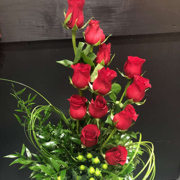 Tall arrangement of red roses with green filler in a white container