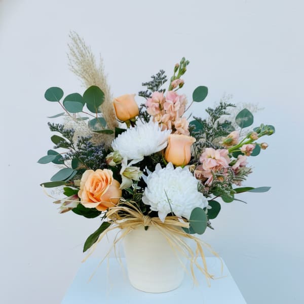 Peach and white floral arrangement in a white vase with eucalyptus